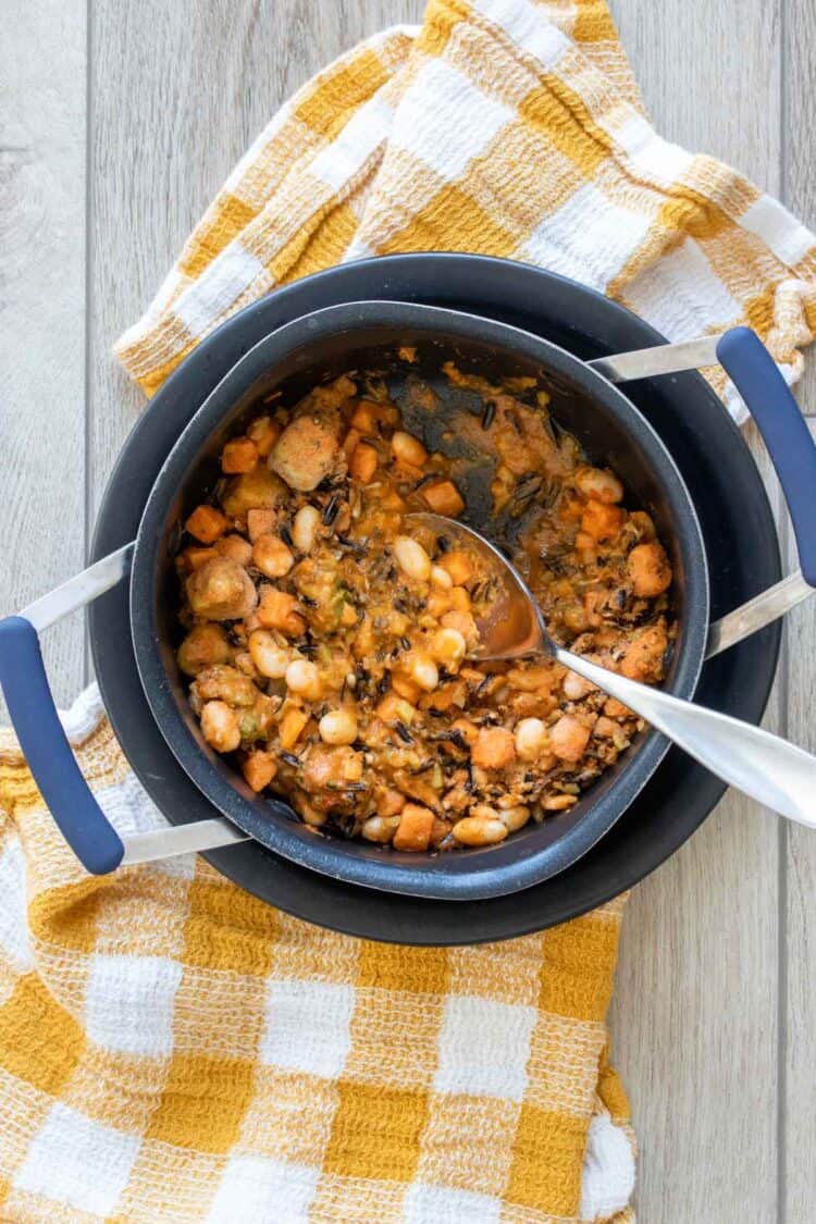 Top view of a spoon mixing a frozen meal with rice and beans in a black pot on a yellow checkered towel