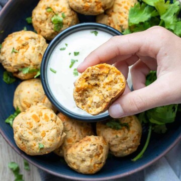 Hand holding a sausage and cheese ball over a plate of more with dip in the center