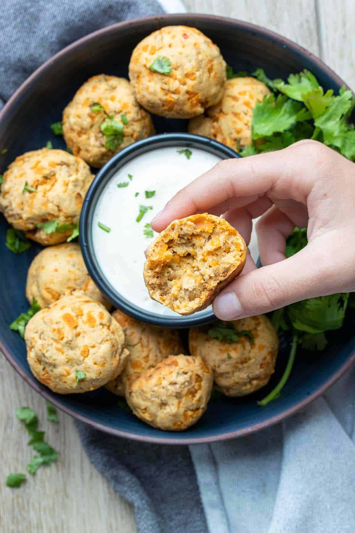 Hand holding a sausage and cheese ball over a plate of more with dip in the center.