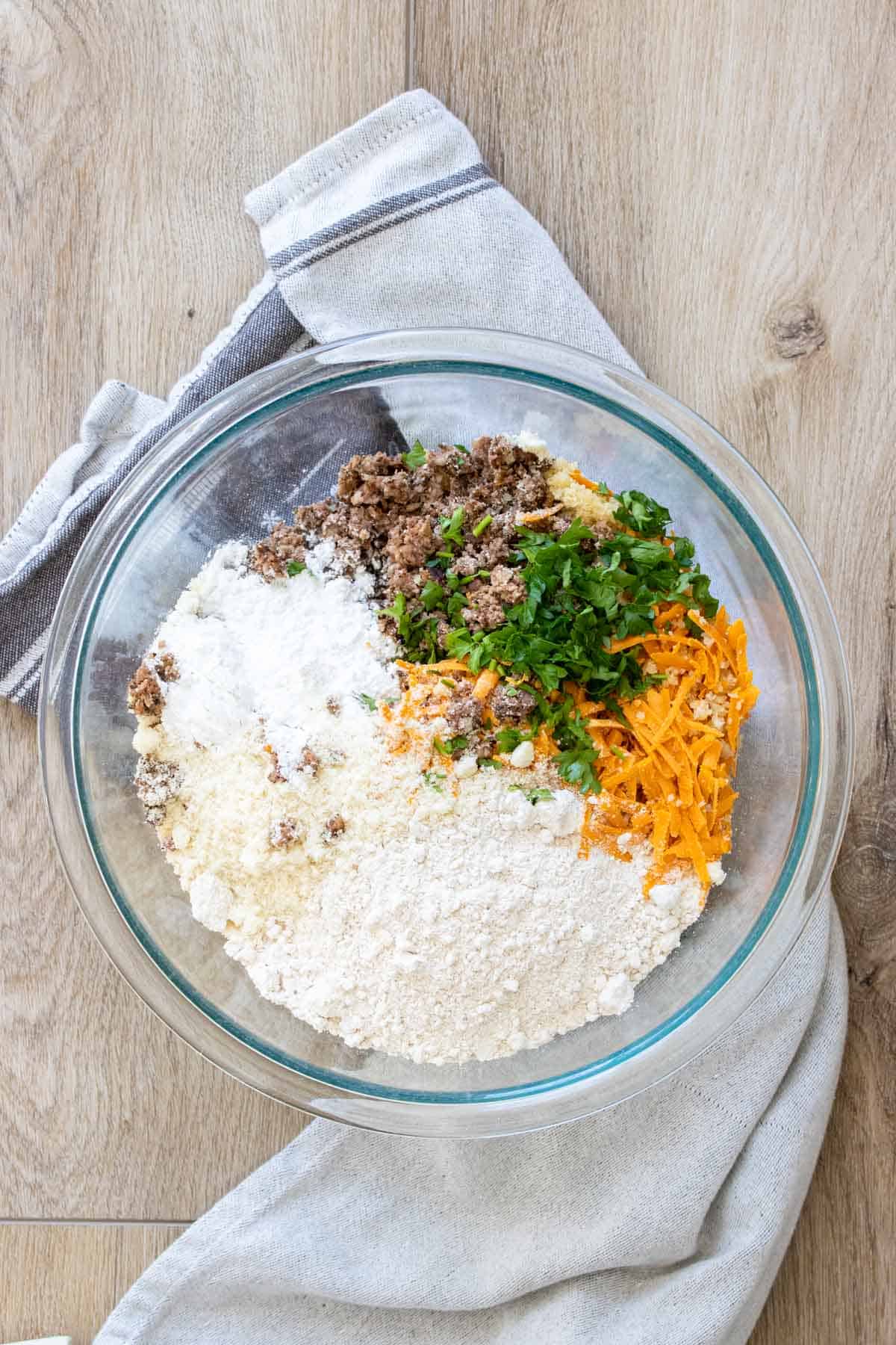 Glass bowl with flours, parsley, shredded cheese and crumbled sausage.