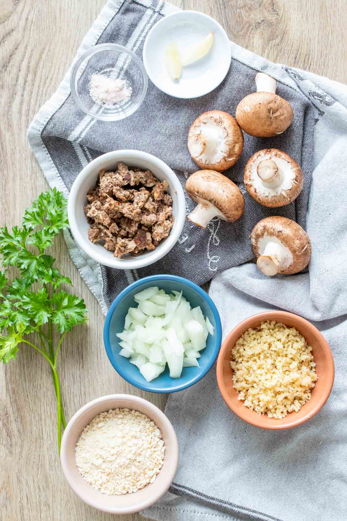 Mushrooms and ingredients needed to stuff them on a grey towel laying on a wooden surface