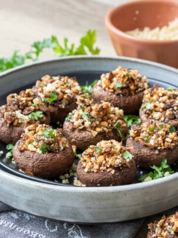 Black plate in a grey plate filled with stuffed appetizer mushrooms with chopped parsley on top