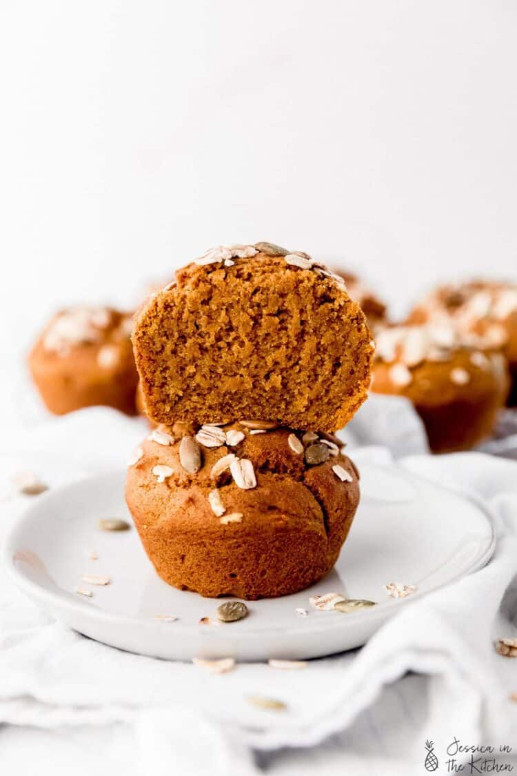 A cut pumpkin muffin on top of a whole one on a white plate