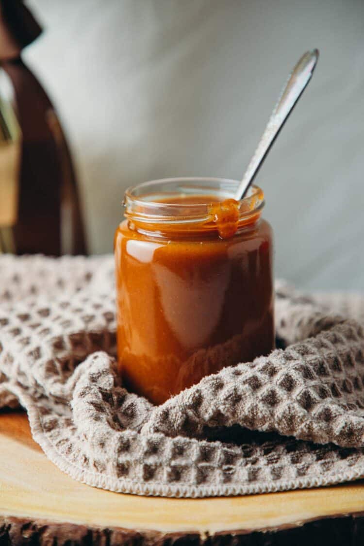 Jar with a dark orange pumpkin sauce in it and a spoon in the sauce