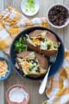 Top view of two baked potatoes loaded with ingredients in a blue shallow bowl on a checkered towel.