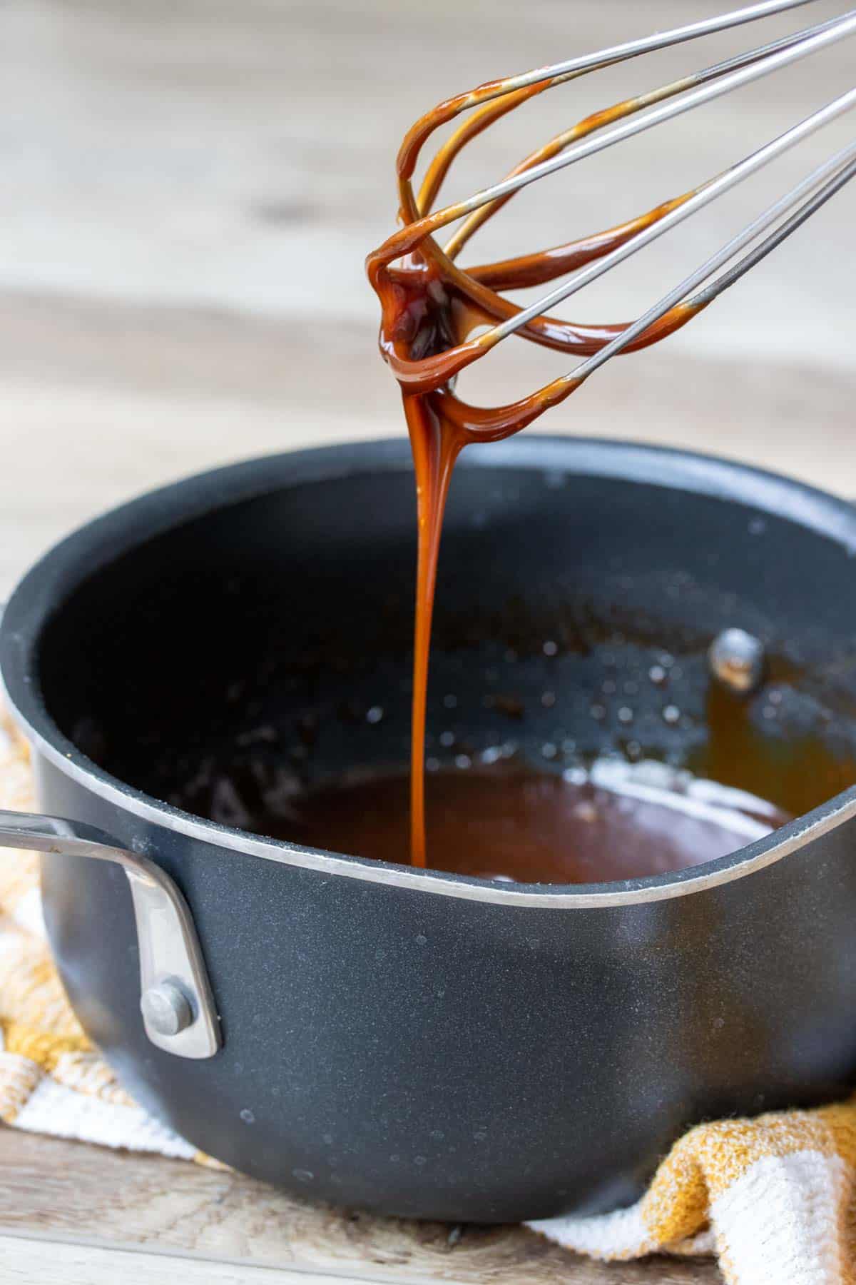 Whisk with caramel dripping off of it into a black pot