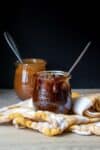 A glass jar with a dark colored caramel sauce dripping off the side in front of a jar with light caramel