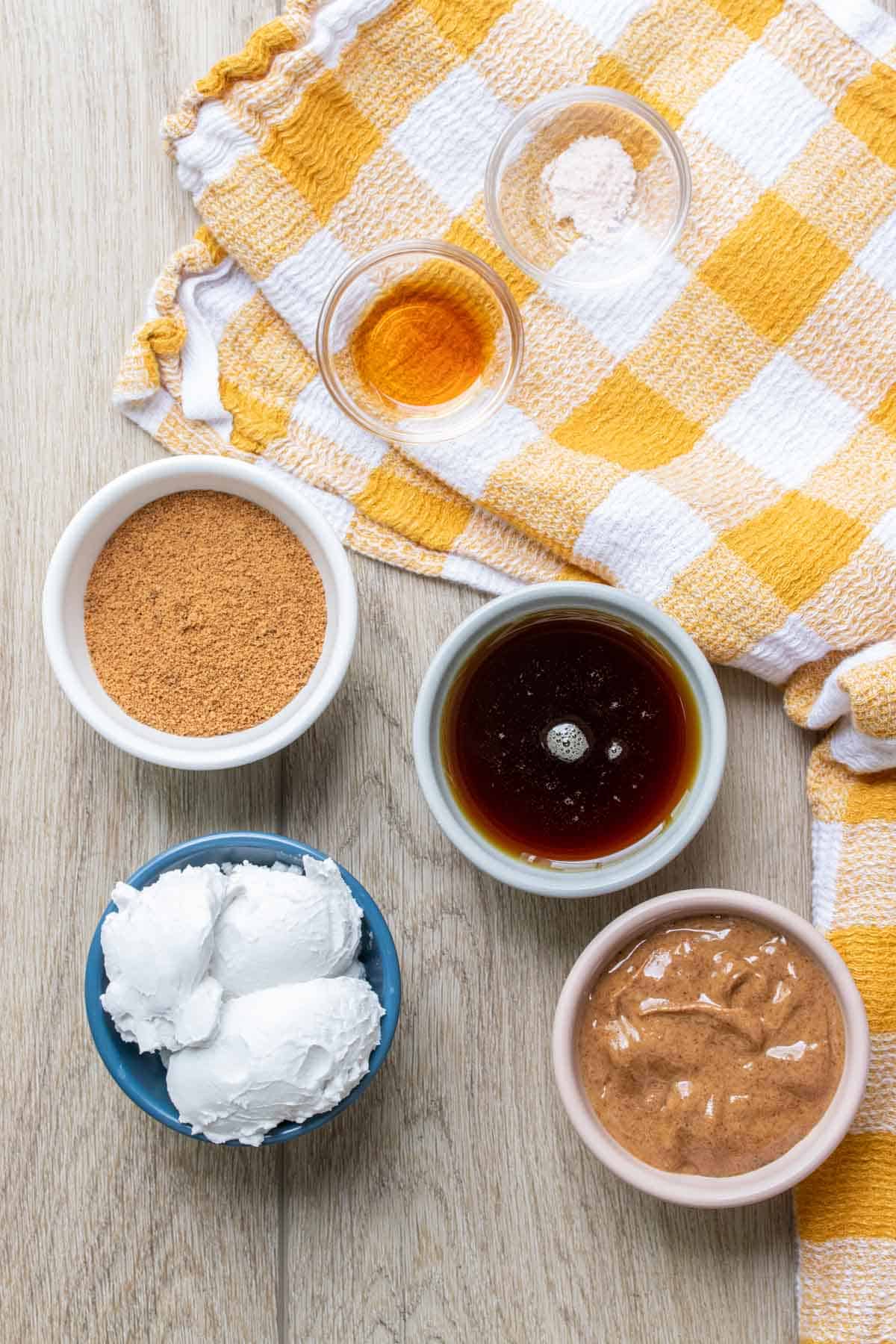 Bowls with coconut cream, maple syrup, almond butter, sugar, vanilla and salt on a yellow towel