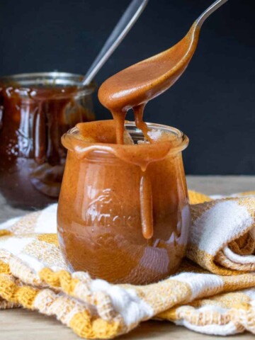 A spoon with caramel coming out of a glass jar filled with it