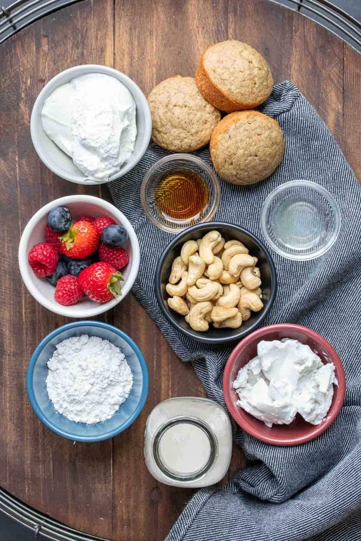 Bowls with berries, cashews, whipped cream, sugar, lemon juice and vanilla next to a jar of milk and cupcakes.