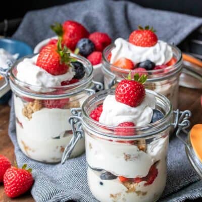 Three glass jars layered with cream, pudding, cake and berries on a wooden tray