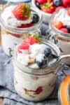 A spoon getting a bite of a layered berry trifle from a glass jar with a hinged lid