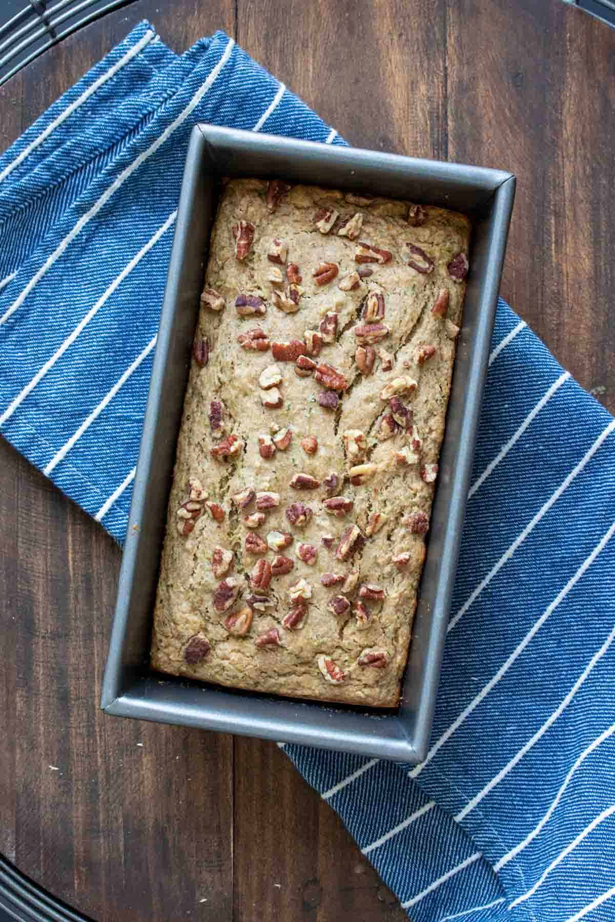 A baked bread loaf topped with nuts in a bread pan