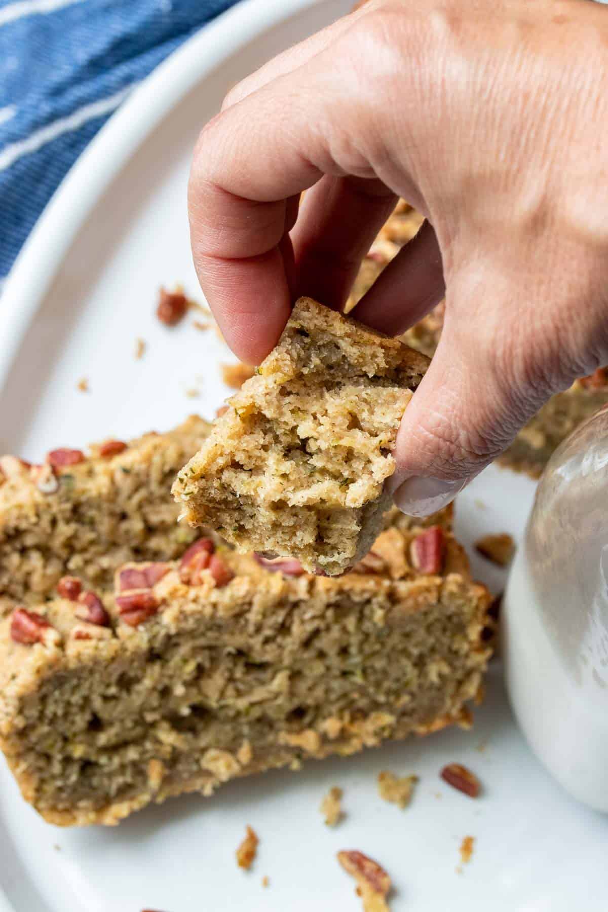 Hand holding a small piece of bread over two slices of the bread on a white plate