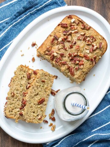 Jar of milk with a straw on a white plate next to slices of bread topped with nuts