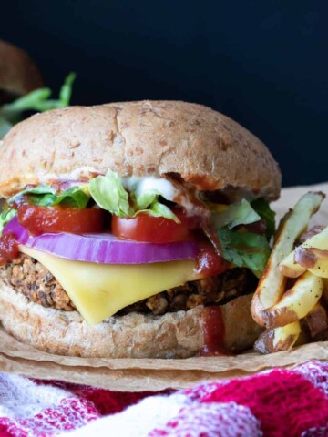 A veggie burger with cheese and toppings on a plate next to fries sitting on a red checkered towel.