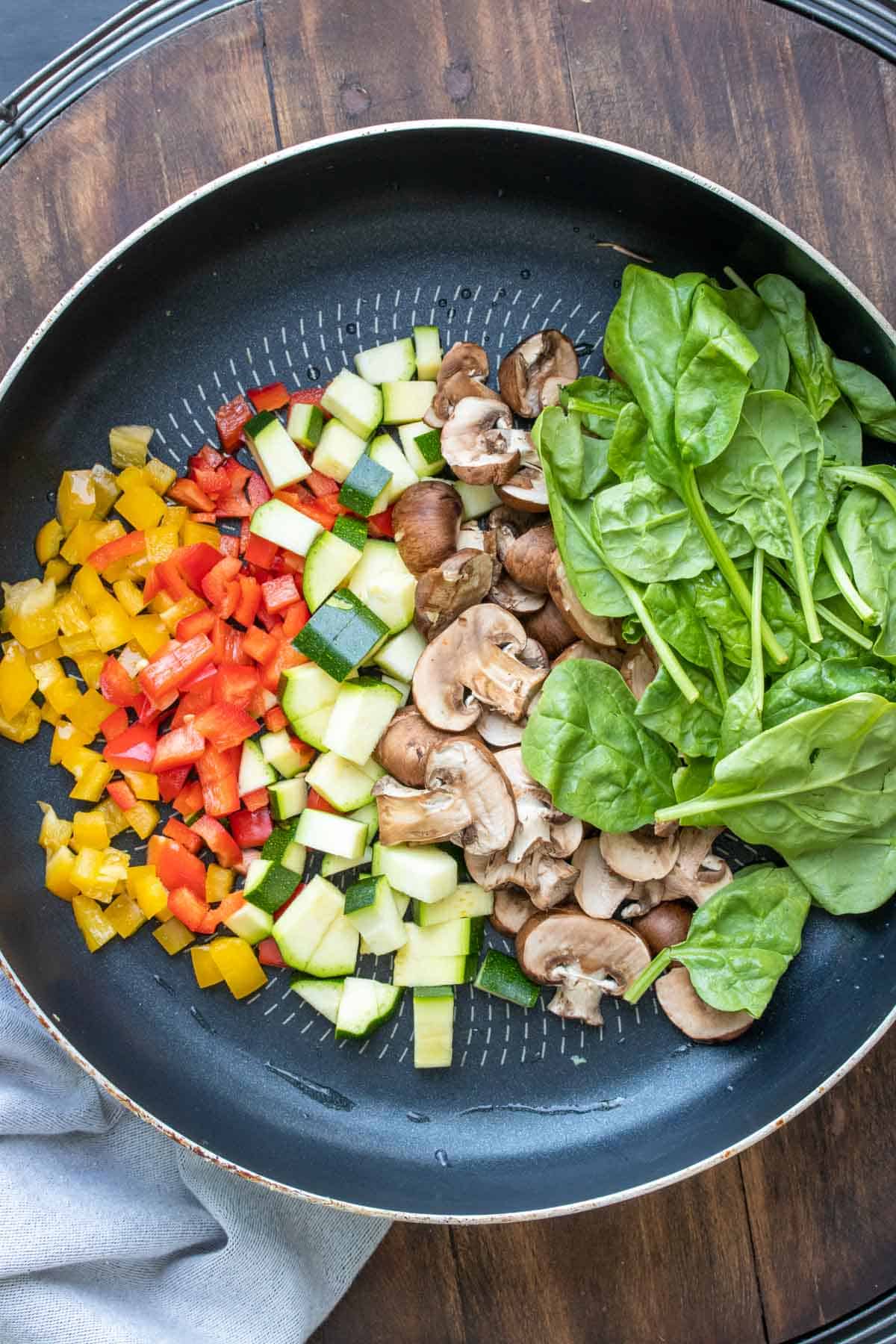 Chopped mushrooms, peppers, zucchini and spinach lined up in a pan
