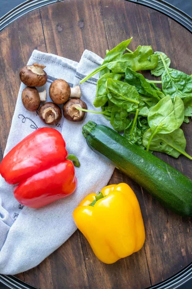 Spinach, mushrooms, peppers and zucchini on a wooden surface