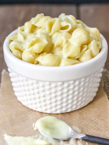 White textured bowl on a piece of brown parchment filled with pasta shells mixed with white cheese sauce