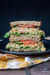 Two pieces of a mashed chickpea salad sandwich sitting on a black plate.