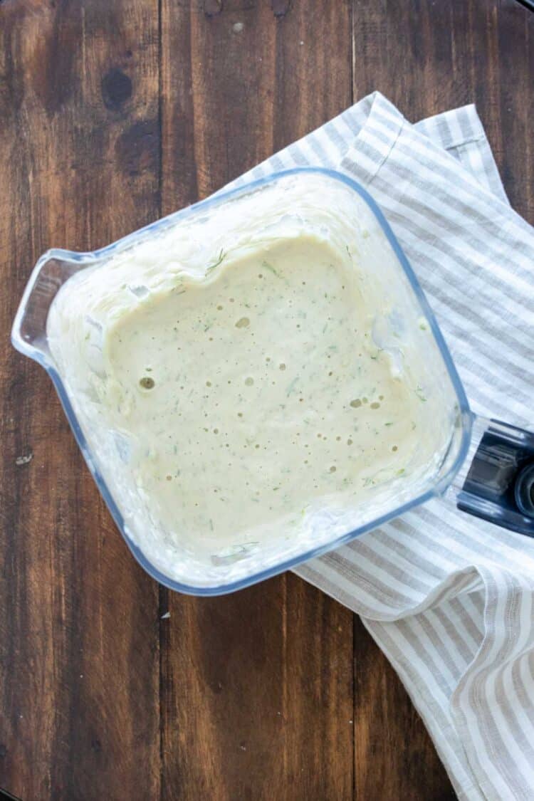 Top view of a blender with a white sauce inside with green specs in it