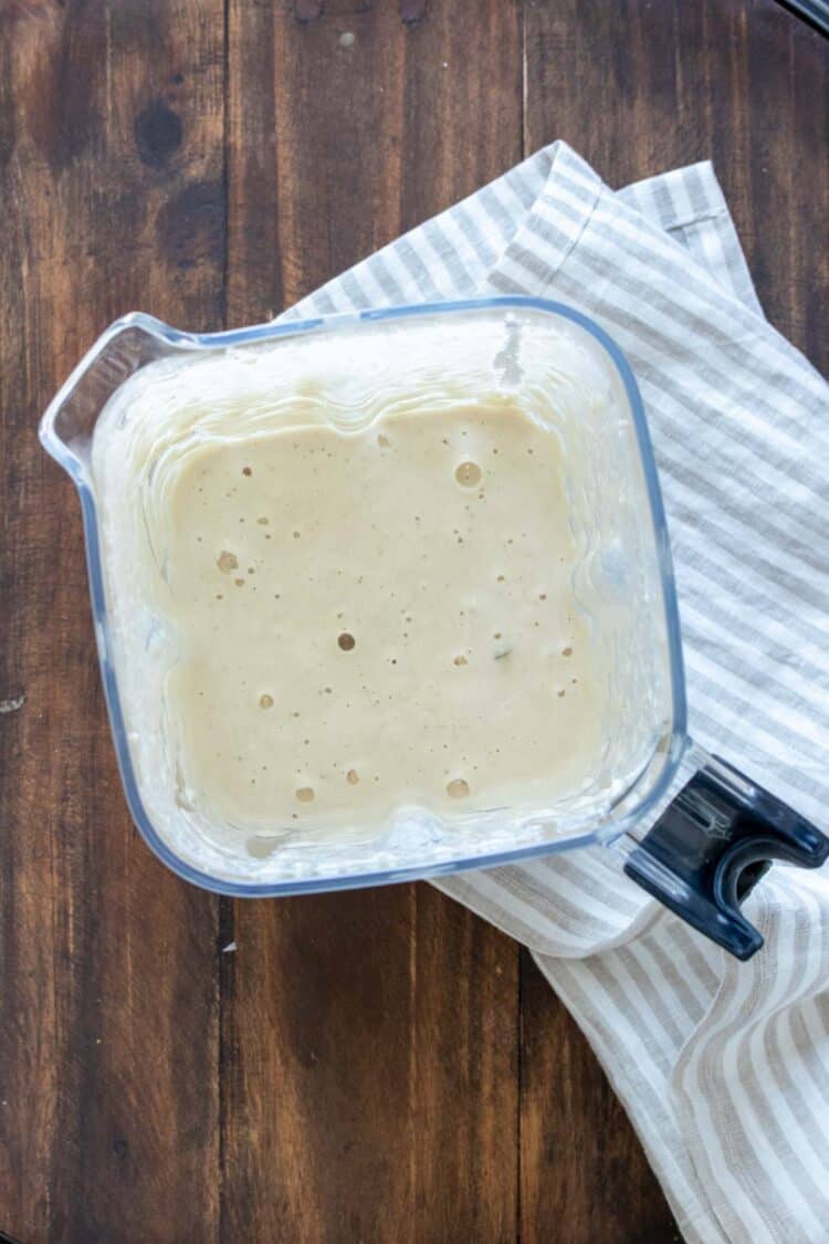 Top view of a blender on a striped towel with a white creamy sauce inside.