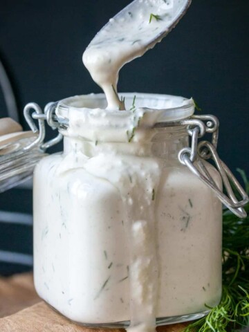 A glass jar filled with tzatziki sauce and a spoon coming out of the top