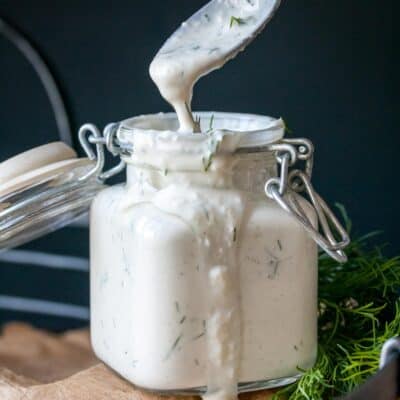 A glass jar filled with tzatziki sauce and a spoon coming out of the top