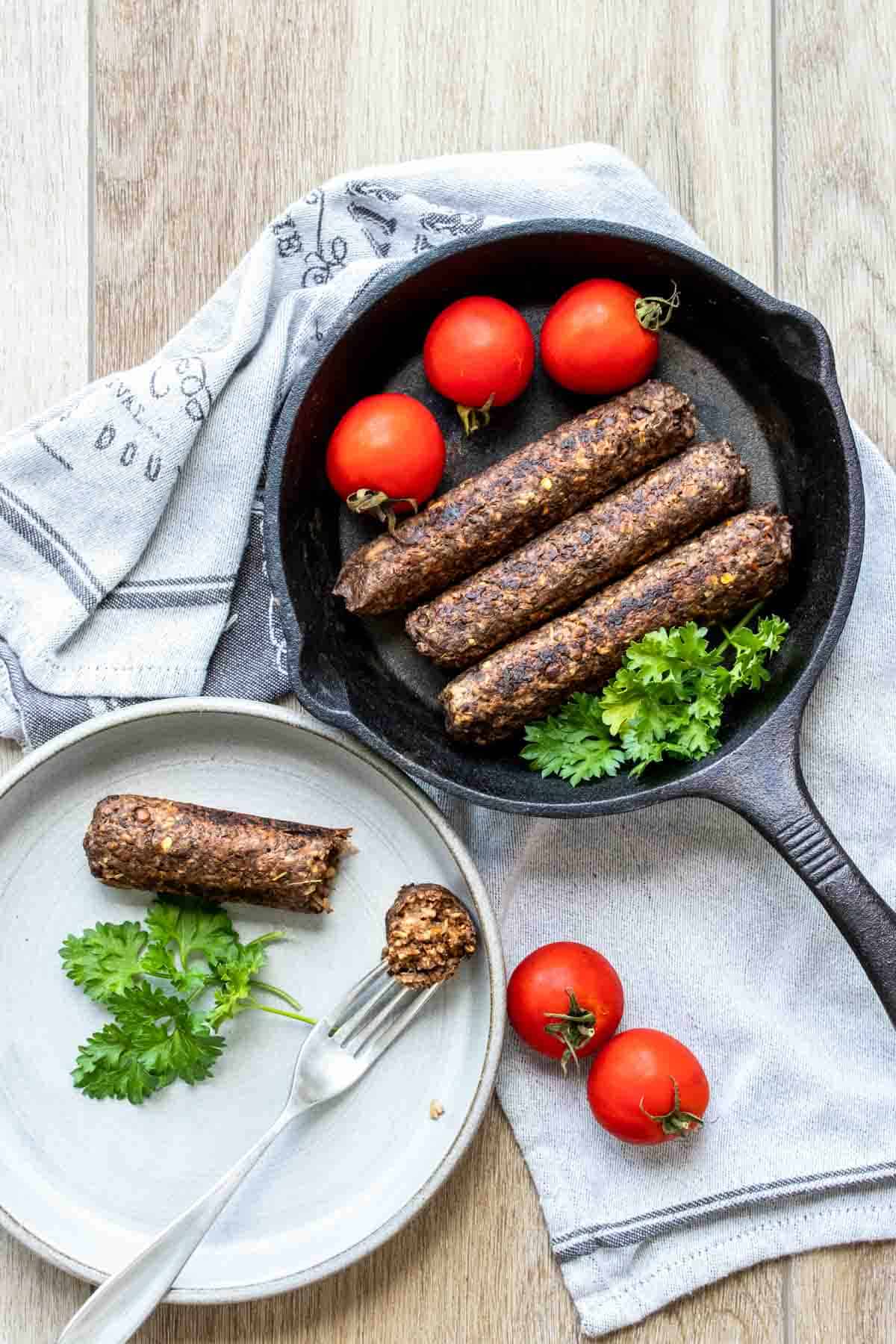 Top view of a cast iron skillet with sausages in it next to a plate with a sausage being eaten
