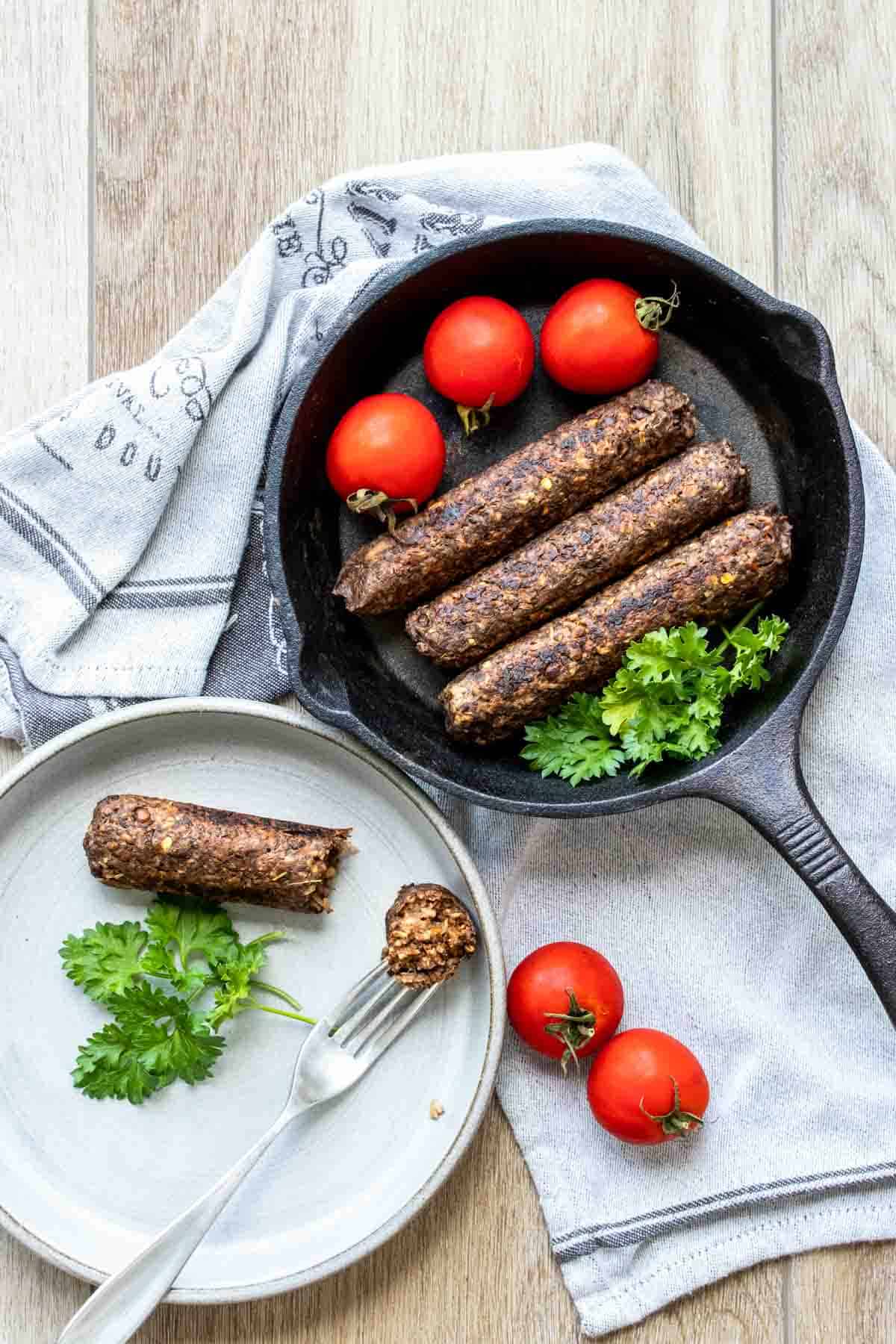 Top view of a cast iron skillet with sausages in it next to a plate with a sausage being eaten.