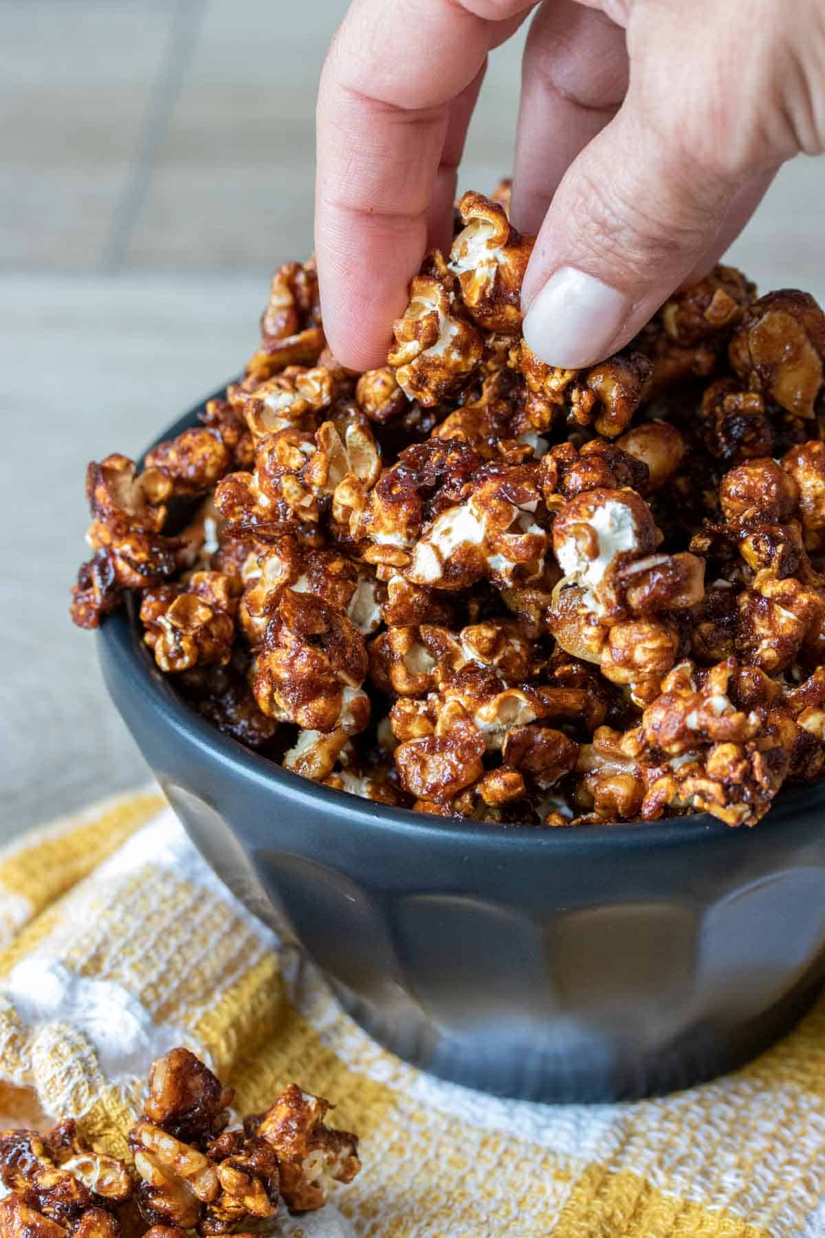 Hand grabbing some caramel popcorn from a black bowl on a yellow towel
