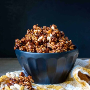 Black bowl overflowing with caramel popcorn sitting on a yellow and white checkered towel