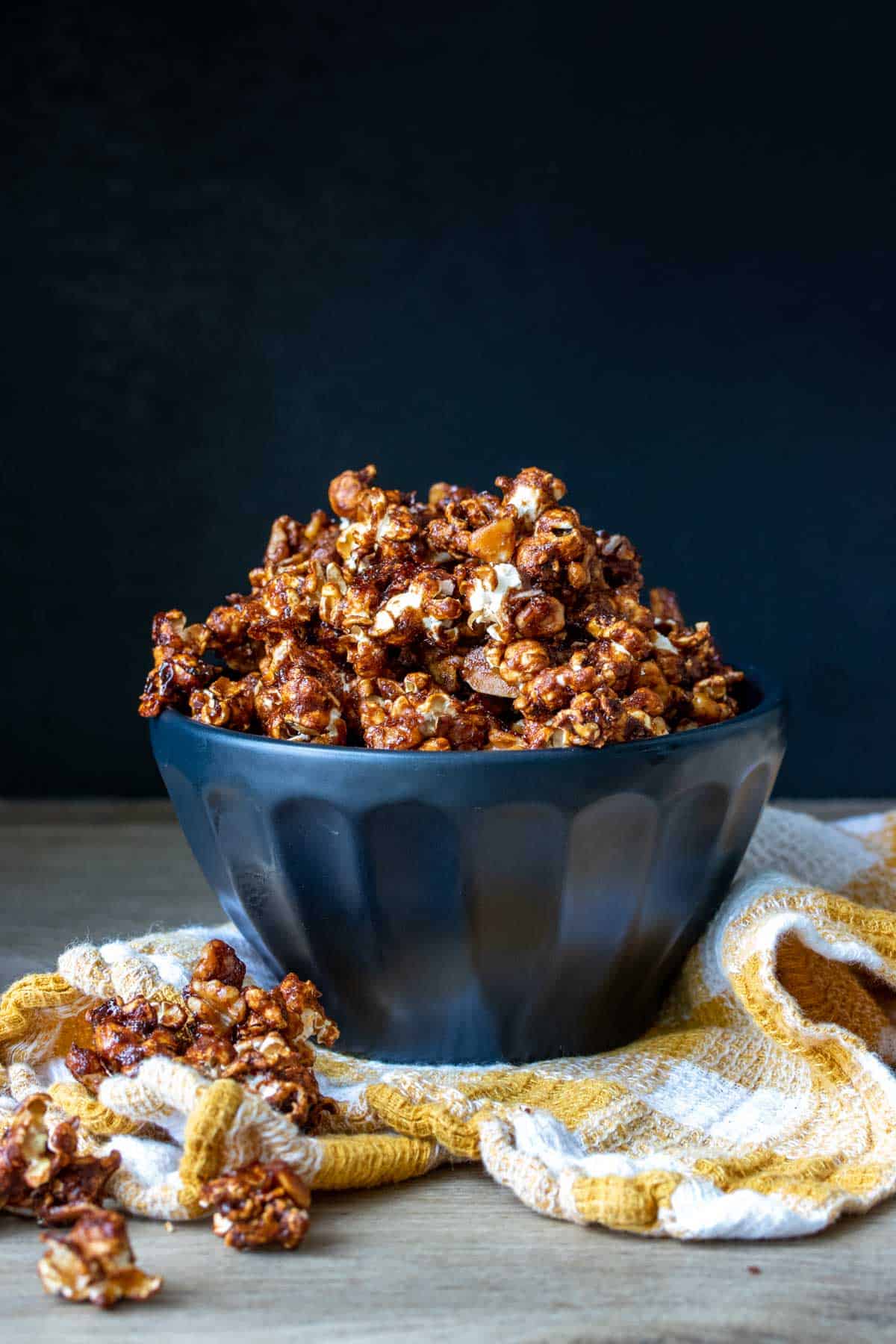 Black bowl overflowing with caramel popcorn sitting on a yellow and white checkered towel