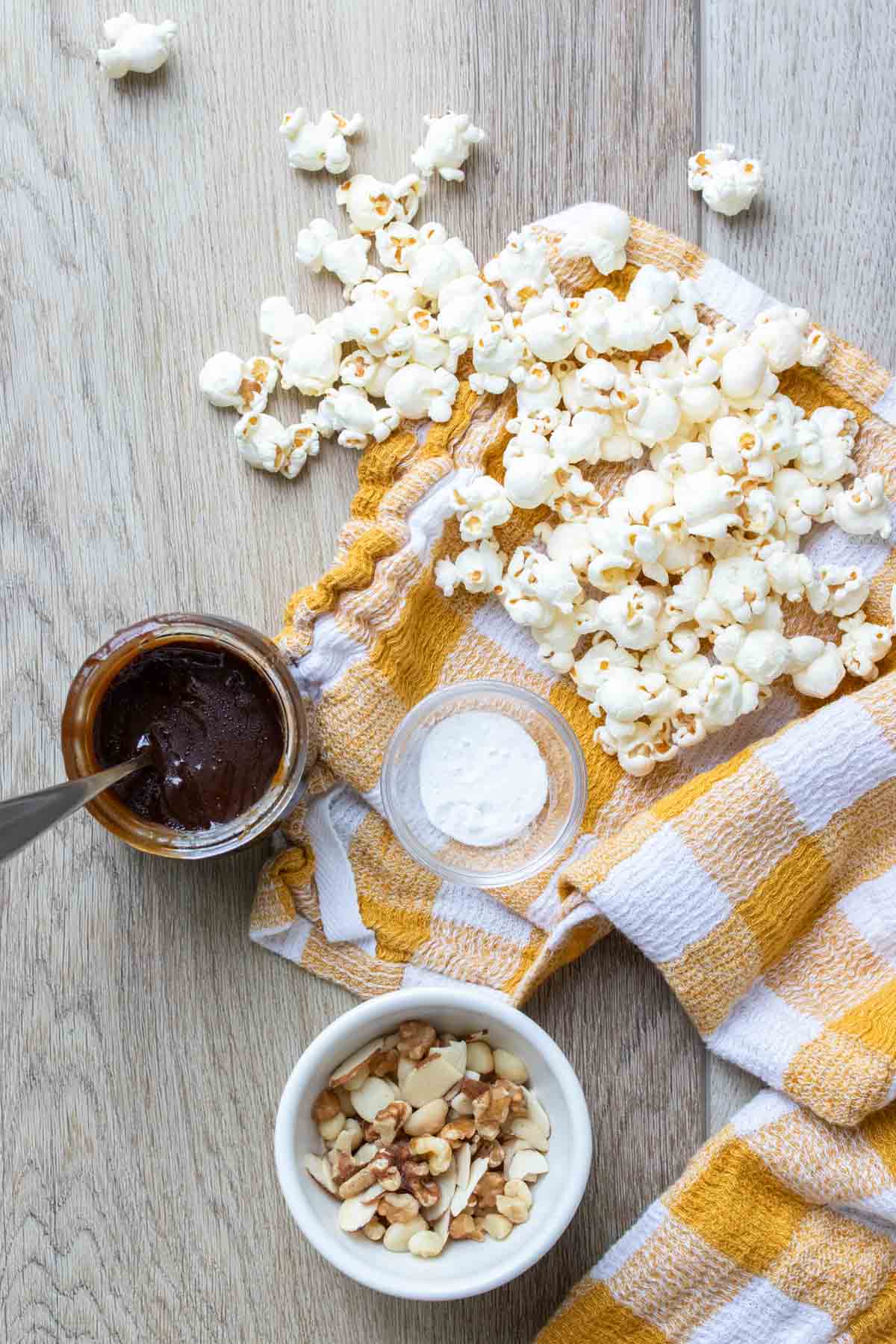 Popcorn, and containers with nuts, caramel and baking soda next to a yellow checkered towel