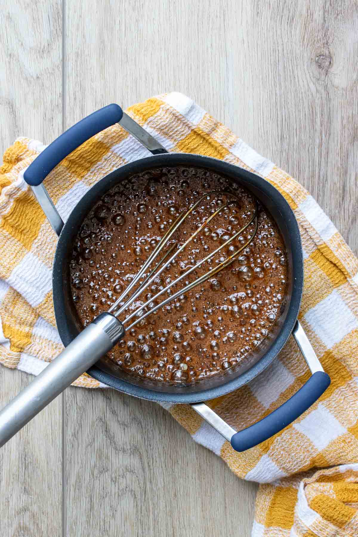 A whisk mixing around caramel in a black pot