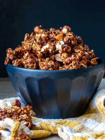 Caramel popcorn piled high in a black bowl with some spilled off the side