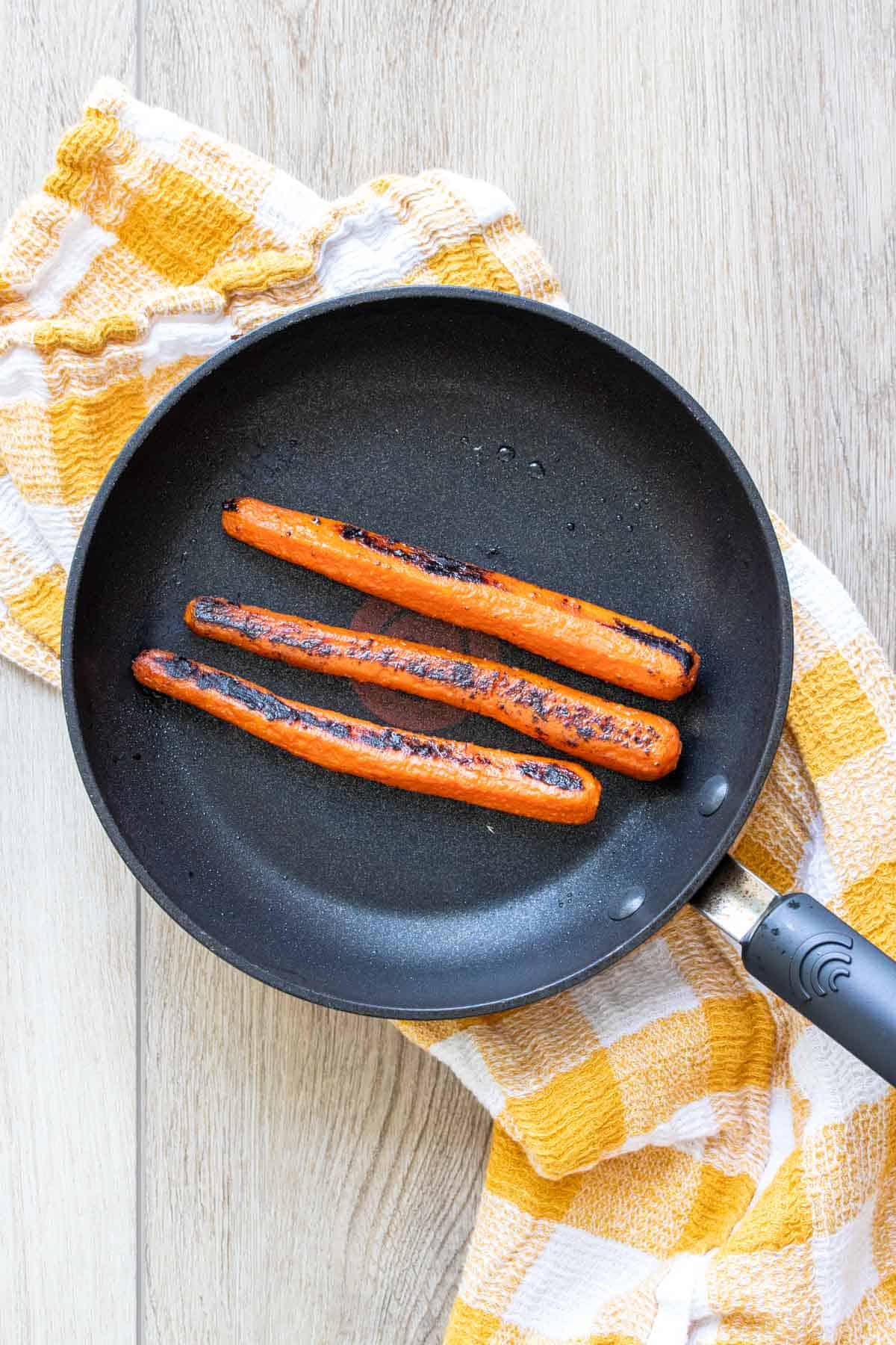 Three carrots being cooked and charred in a pan