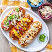 A white plate with three carrot dogs in buns and covered by toppings