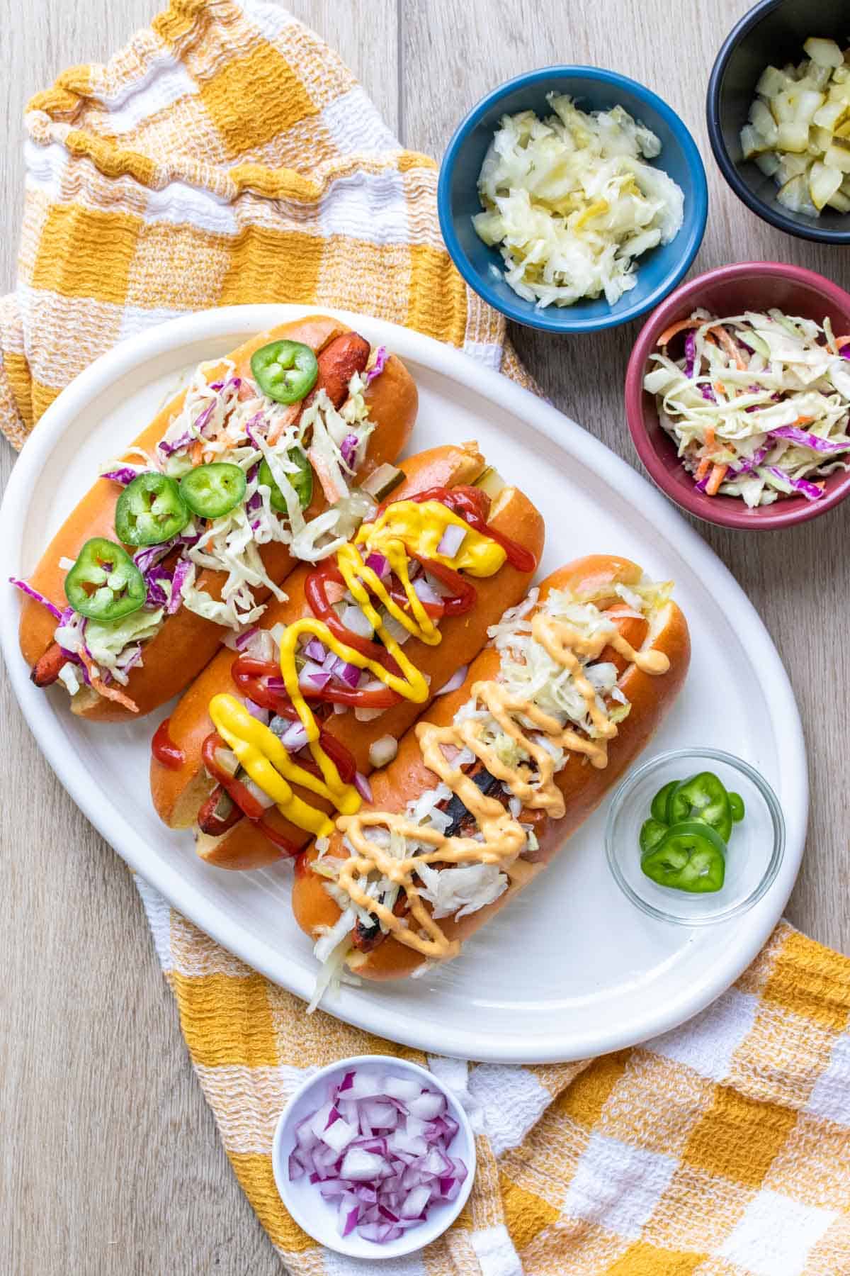 A white plate with three carrot dogs in buns and covered by toppings