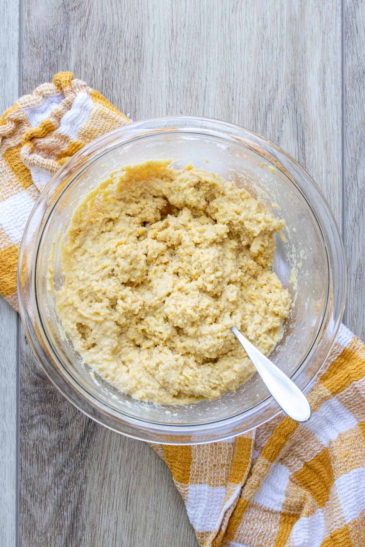 Spoon mixing a wet cornmeal mixture in a glass bowl