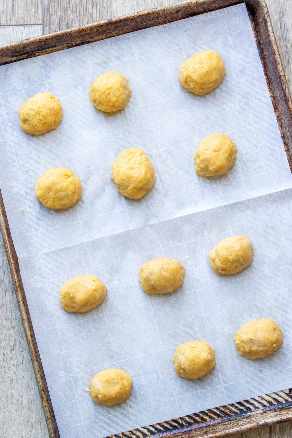 Raw pieces of corndogs on a parchment lined cookie sheet