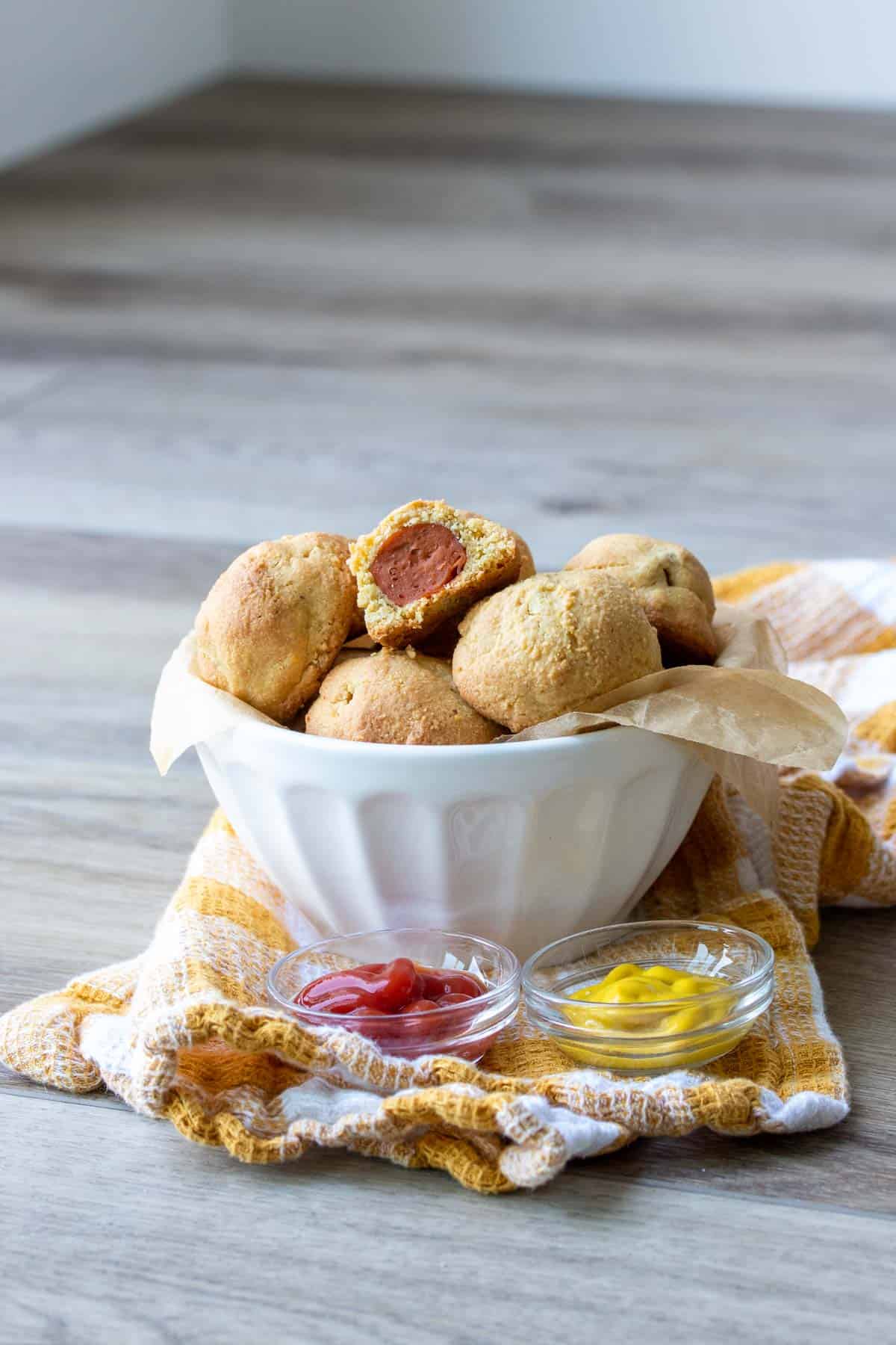 White bowl with corn dog bites piled in next to ketchup and mustard
