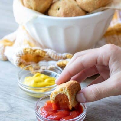 Hand dipping a corn dog with a bite into ketchup