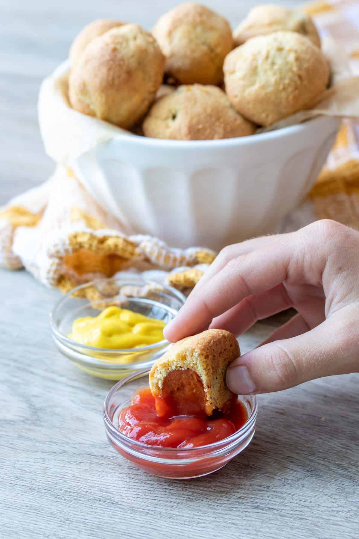 Hand dipping a corn dog with a bite into ketchup