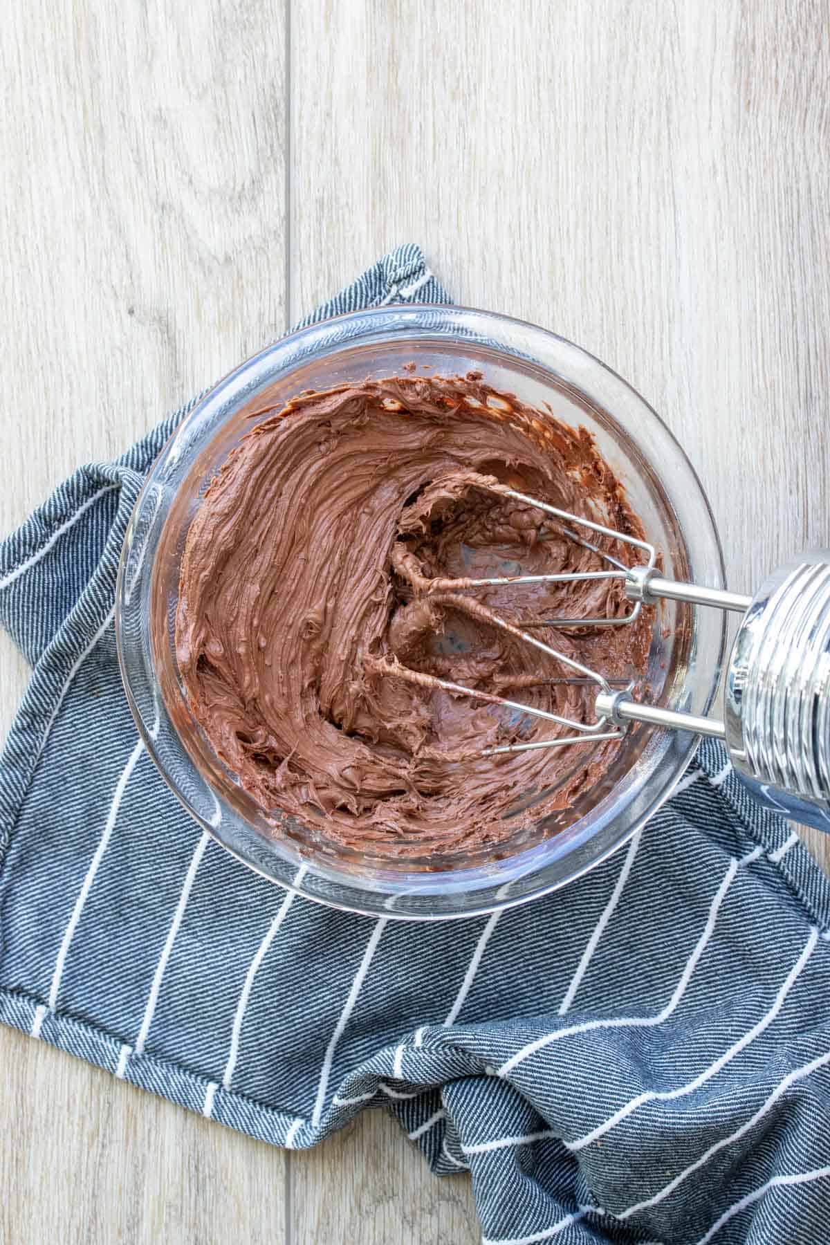 Hand beater mixing chocolate frosting in a glass bowl