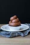 A chocolate cupcake with swirled chocolate frosting on a white plate