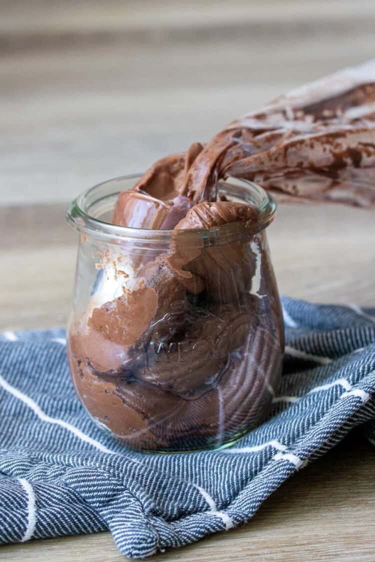 A plastic bag with chocolate frosting in a glass jar filled with frosting