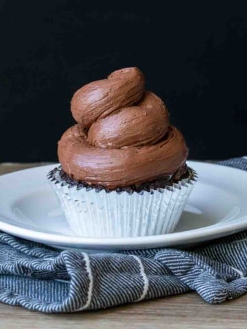 Swirled chocolate frosting on a cupcake sitting on a white plate.