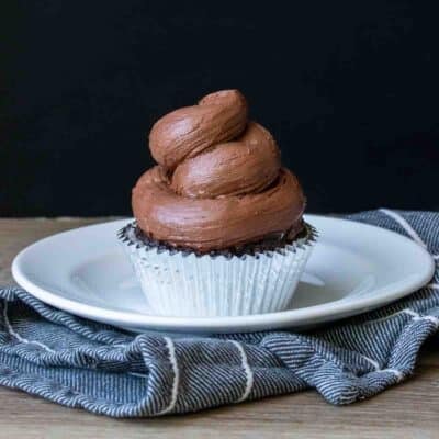 Swirled chocolate frosting on a cupcake sitting on a white plate