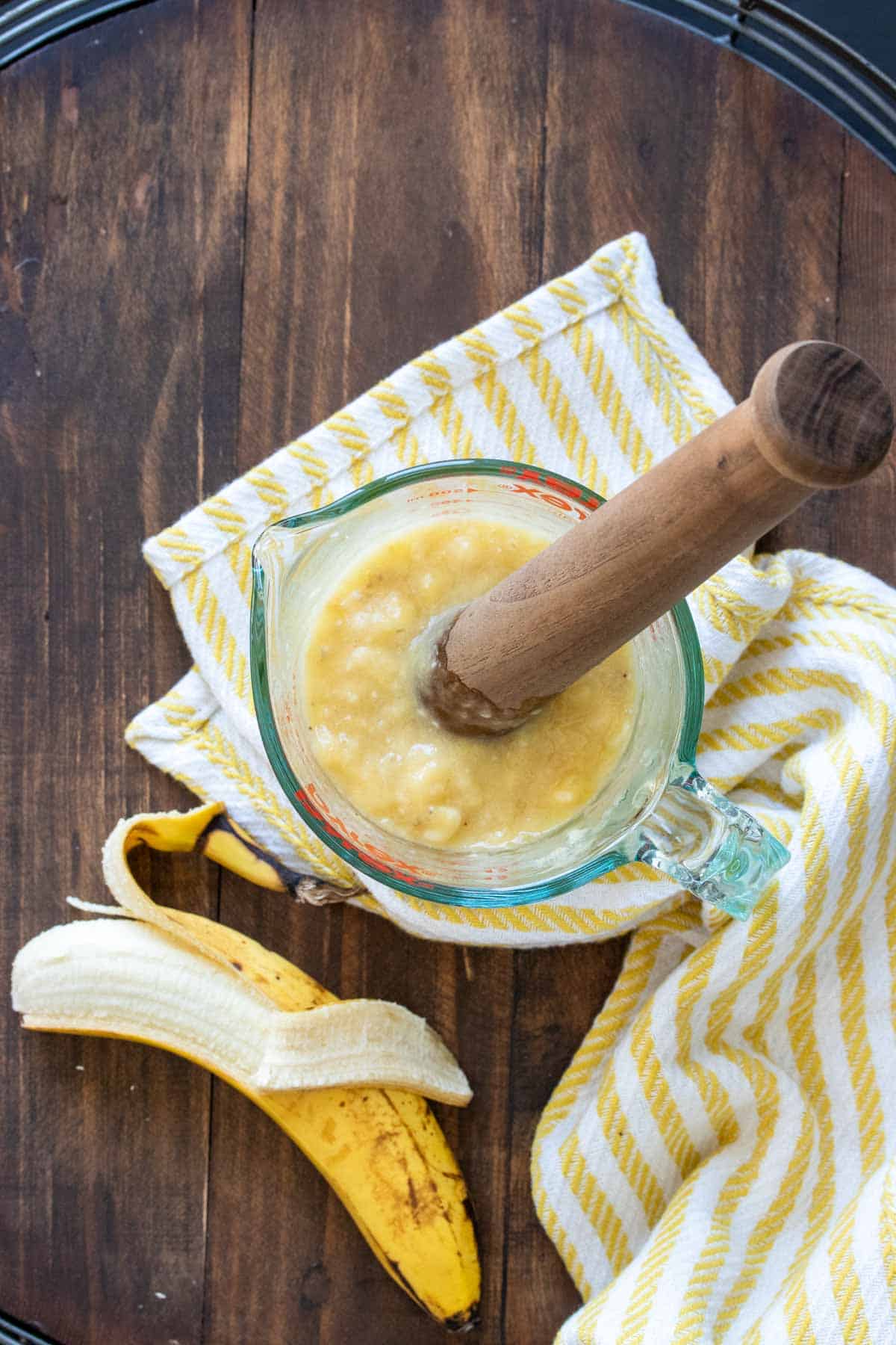 A wooden mortar mushing banana in a glass measuring bowl